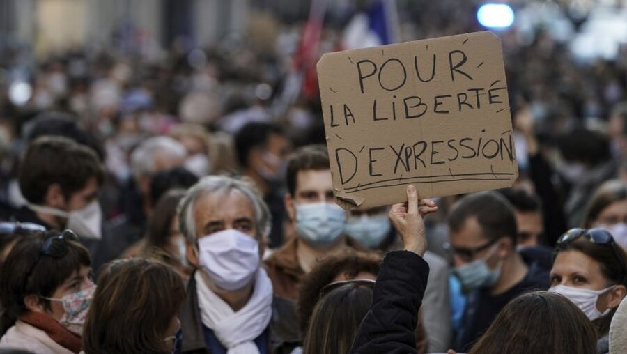 Ein Protestteilnehmer in Lyon hält ein Plakat hoch, auf dem zu lesen ist (Pour la liberté d'expression) "Für die Redefreiheit". / © Laurent Cipriani/AP (dpa)
