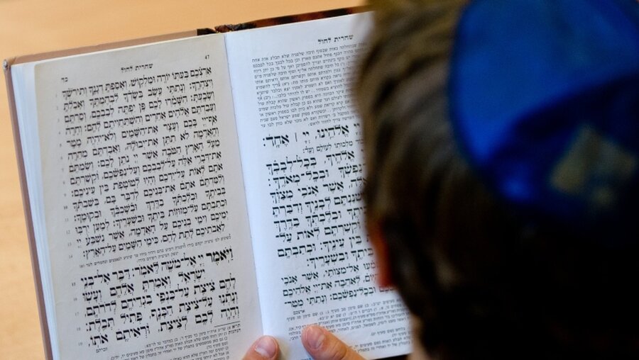 Ein Schüler mit Kippa schaut in ein jüdisches Gebetsbuch.  / © Daniel Bockwoldt (dpa)