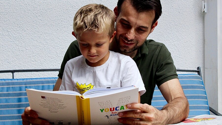 Ein Vater liest mit seinem Kind im "Youcat for Kids" (YouCat)