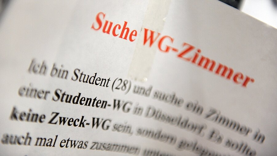 Ein Zettel mit der Aufschrift "Suche WG-Zimmer" hängt an einem Schwarzen Brett in der Universität in Düsseldorf / © Daniel Naupold (dpa)