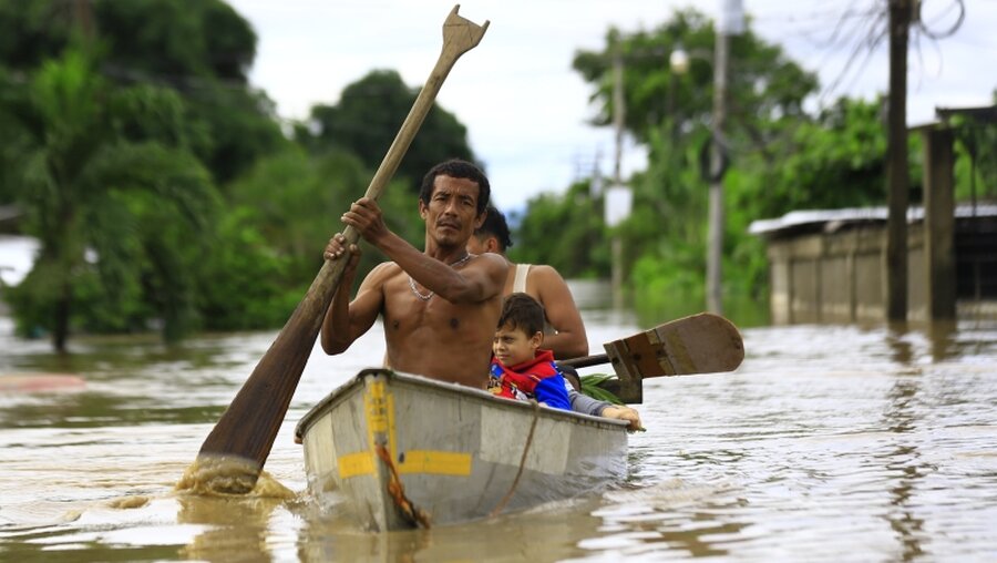 Eine Familie fährt mit einem Kanu durch eine überschwemmte Straße / © Stringer (dpa)
