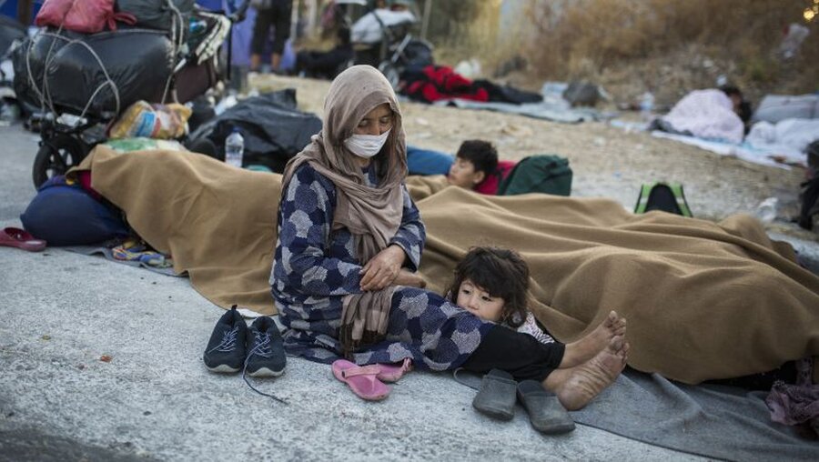 Eine Frau mit ihren Kindern sitzt am Rande einer Straße in der Nähe des ausgebrannten Flüchtlingslagers Moria / © Socrates Baltagiannis (dpa)