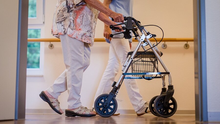 Eine Pflegekraft geht in einem Pflegeheim mit einer älteren Dame / © Christoph Schmidt (dpa)