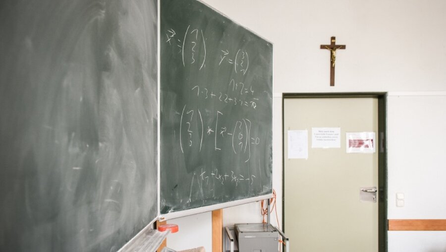 Eine Schultafel in einem Klassenraum mit Kreuz über der Tür / © Julia Steinbrecht (KNA)