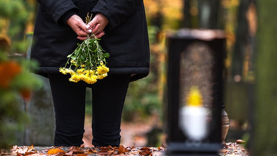 Eine trauernde Frau steht mit Blumen in der Hand an einem Grab. / © encierro (shutterstock)
