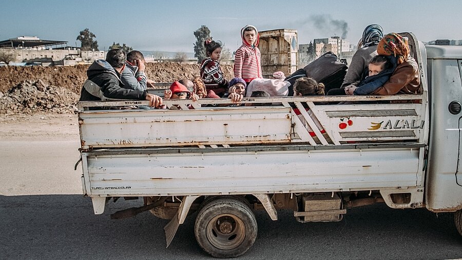 Erwachsene und Kinder sitzen mit Gepäck auf der Ladefläche eines Transporters und fliehen / © Emilie Buzyn (KNA)