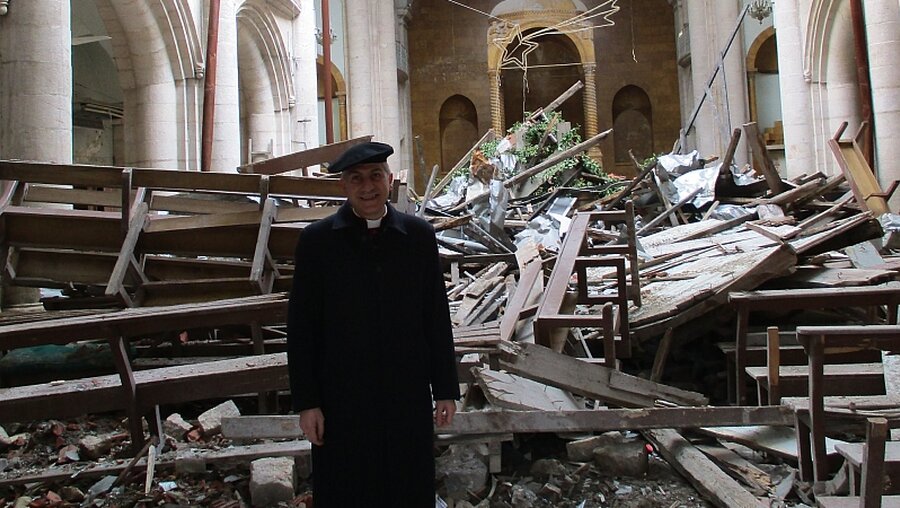 Erzbischof Joseph Tobji steht in einer zerstörten Kirche in Aleppo. (KiN)