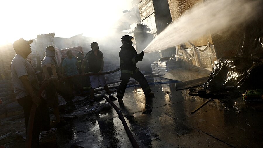 Feuerwehrleute löschen in einem von Demonstranten in Brand gesetzten Laden / © Mario Davila (dpa)
