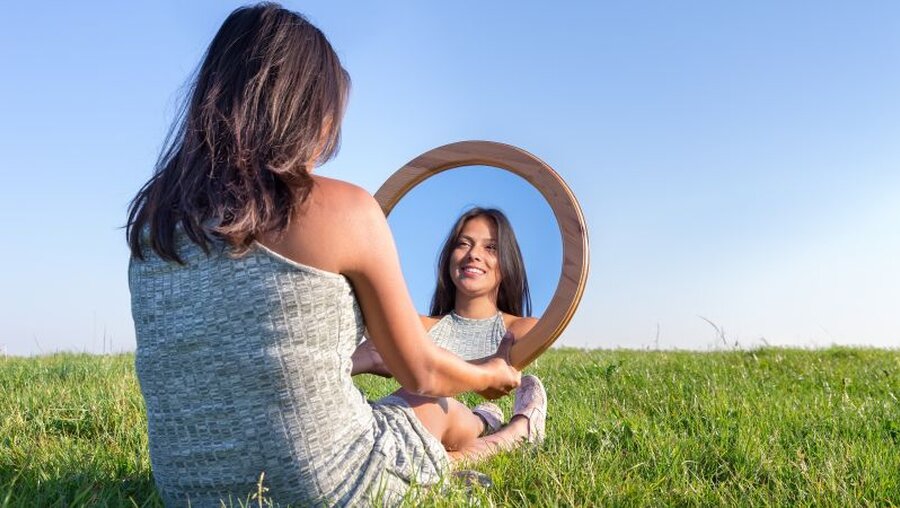 Frau betrachtet sich im Spiegel  (shutterstock)