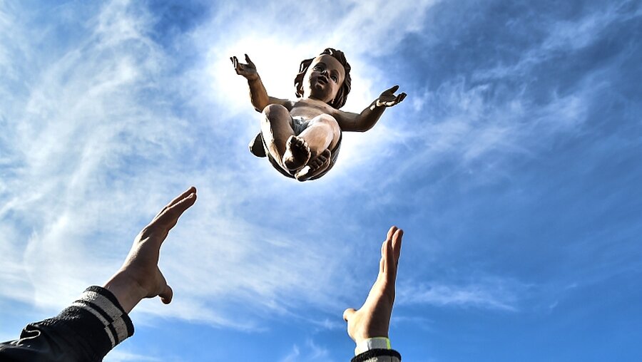 Hände werfen die Figur eines Jesuskinds in die Luft / © Cristian Gennari (KNA)