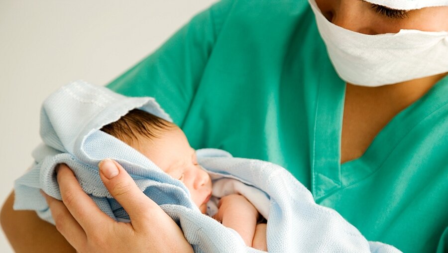 Hebamme hält ein Baby auf dem Arm / © Air Images (shutterstock)