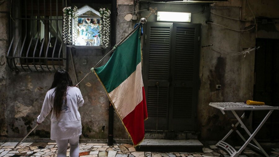 Ein in weiß gekleidetes Mädchen mit italienischer Flagge steht vor einer Hauswand mit einem Marienaltar / © Adelaide Di Nunzio (KNA)