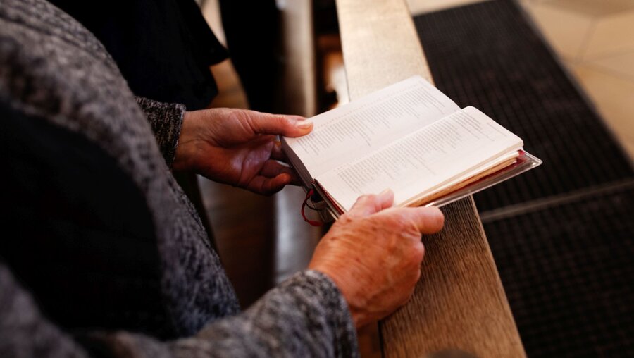 Eine Frau liest im Gesangsbuch im Gottesdienst / © Simon Koy (KNA)