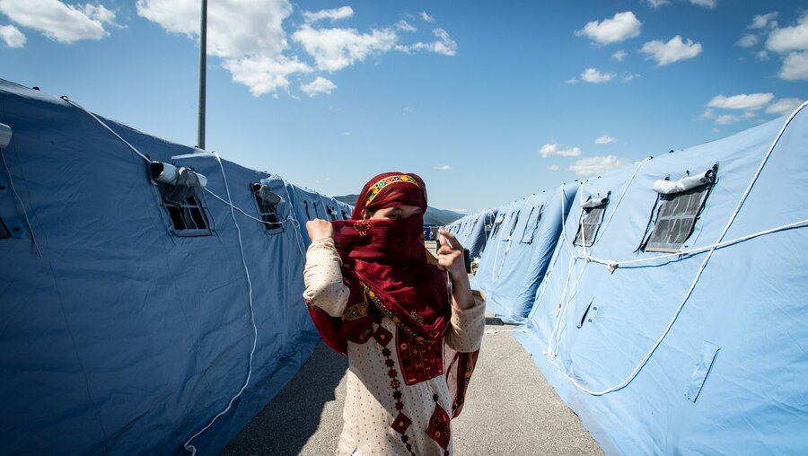 Eine afghanische Frau in Landestracht steht zwischen Zelten und verdeckt ihr Gesicht in einem Flüchtlingscamp für Geflüchtete aus Afghanistan / © Cristian Gennari/Romano Siciliani (KNA)