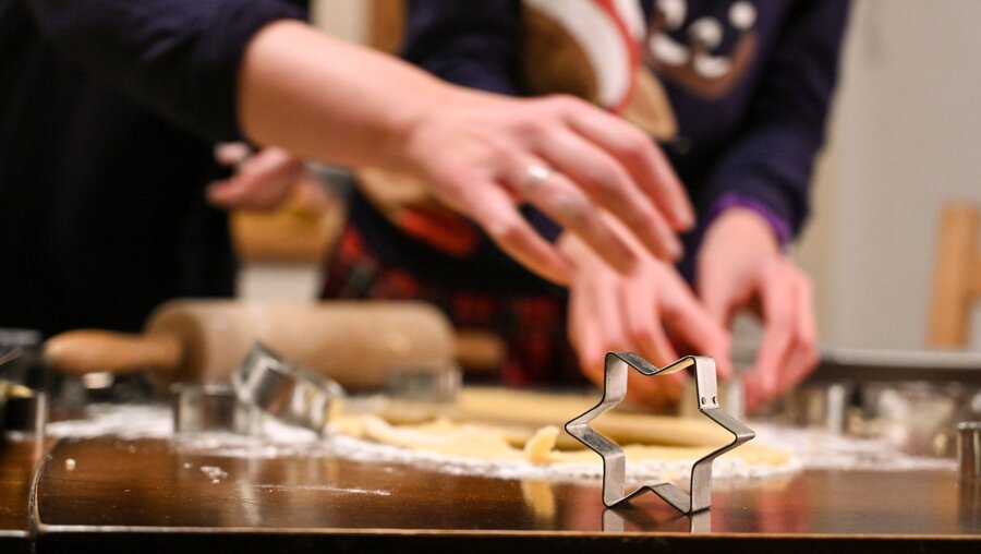 Die Ausstechform für einen Stern steht auf einem Tisch, dahinter ist Teig ausgerollt und Hände stechen Weihnachtsplätzchen aus / © Harald Oppitz (KNA)