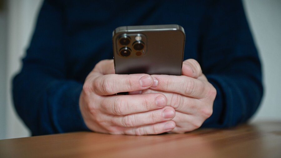 Ein Mann hält ein Smartphone in seinen Händen. / © Julia Steinbrecht (KNA)