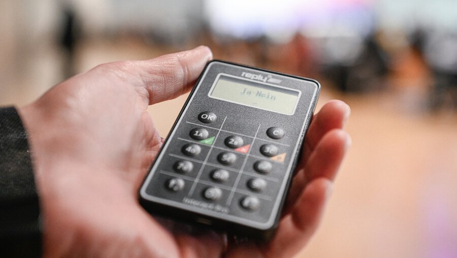 Eine Hand hält ein Gerät für die digitale Abstimmung am 5. Februar 2022 in Frankfurt. / © Julia Steinbrecht (KNA)