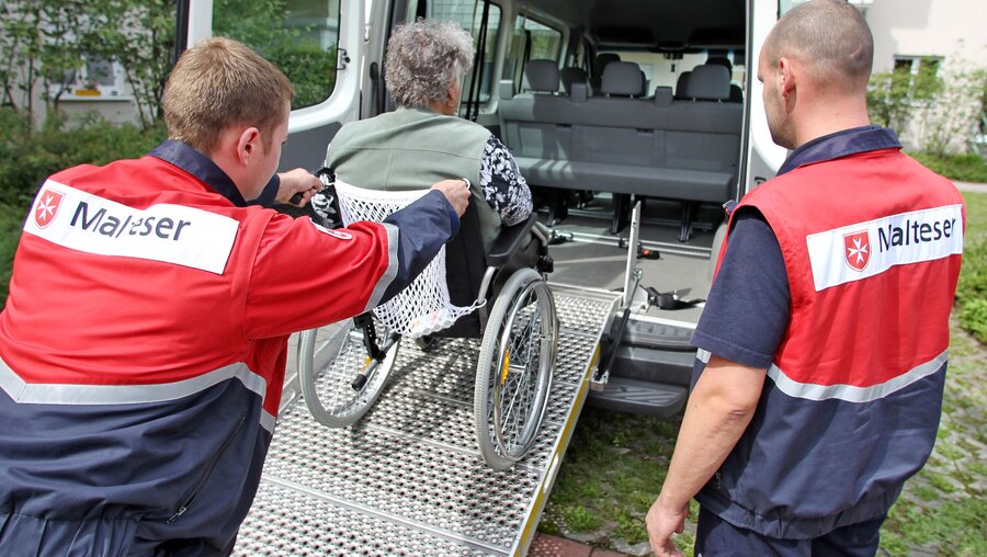 Zwei Freiwillige kümmern sich um eine Dialysepatientin im Rollstuhl / © Jan Woitas (dpa)