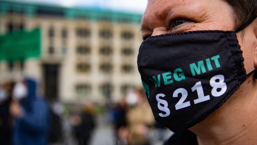 Demonstrantin mit der Schriftzug Weg mit §218 auf einer Maske / © Paul Zinken (dpa)