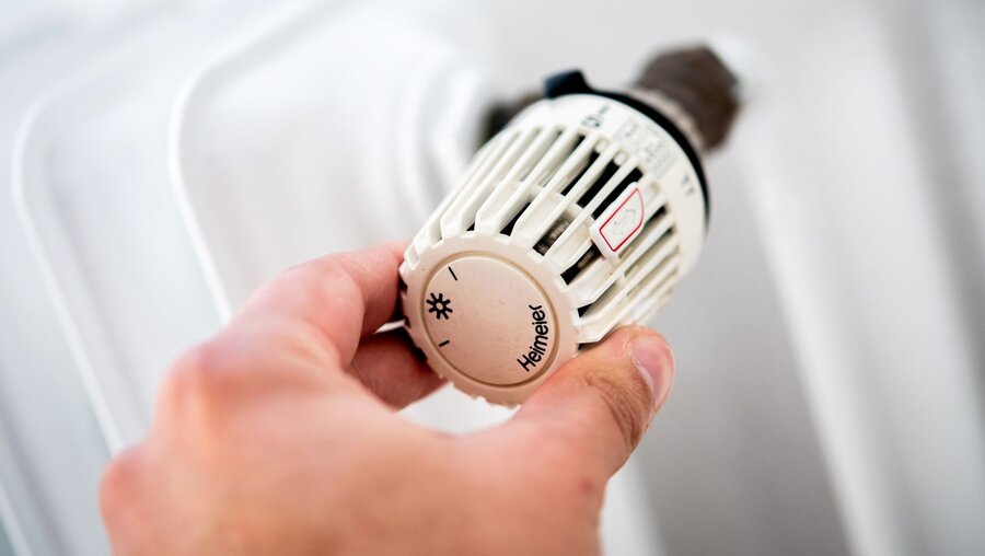 Ein Mann dreht in einer Wohnung am Thermostat einer Heizung / © Hauke-Christian Dittrich (dpa)
