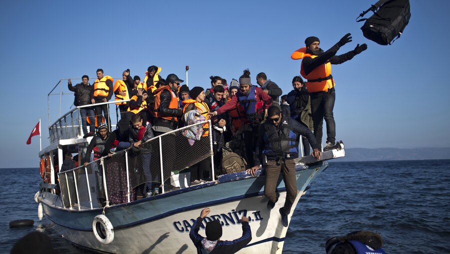 Freiwillige Helfer entladen ein Holzboot mit Flüchtlingen, das gerade von der Türkei am Strand von Lesbos angekommen ist, am 7. November 2015. / © Marko Drobnjakovic (KNA)
