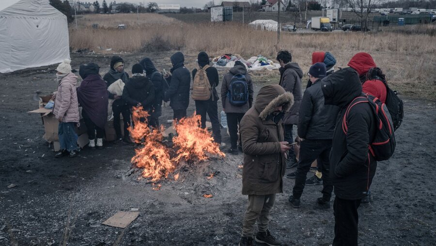 Geflüchtete schützen sich vor der Kälte mit dicken Jacken und Kapuze und stehen um ein Feuer herum am polnisch-ukrainischen Grenzübergang im polnischen Dorf Medyka an der Grenze zur Ukraine / © Francesco Pistilli (KNA)
