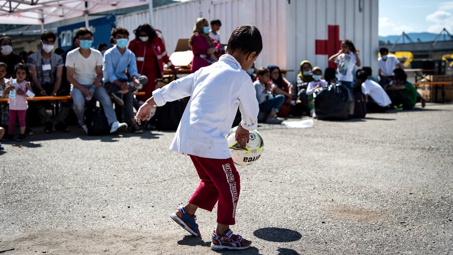 Ein Kind spielt mit einem Ball, davor sind Flüchtlinge und Helfer des italienischen Roten Kreuzes versammelt, in einem Flüchtlingscamp für Geflüchtete aus Afghanistan am 2. September 2021 in Avezzano, Italien. / © Cristian Gennari/Romano Siciliani (KNA)