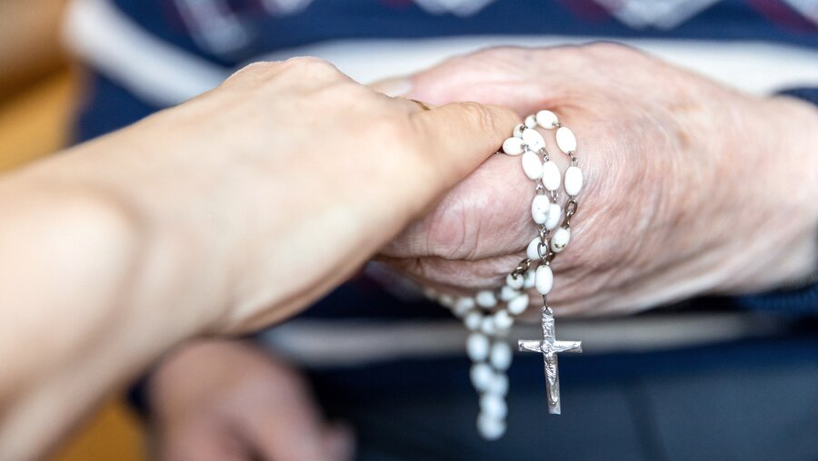Die Hand eines Seniors, um die ein Rosenkranz gewickelt ist, hält eine junge Hand am 16. März 2022 im Caritas Altenpflegeheim Sankt Barbara in Zwickau. / © Lorenz Lenk (KNA)