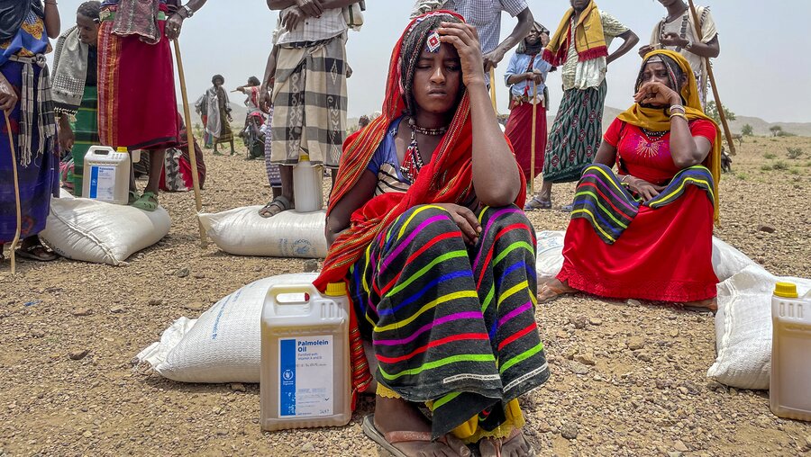 Menschen sitzen und stehen auf Säcken mit Lebensmitteln, die vom Welternährungsprogramm der Vereinten Nationen / © Claire Nevill (dpa)