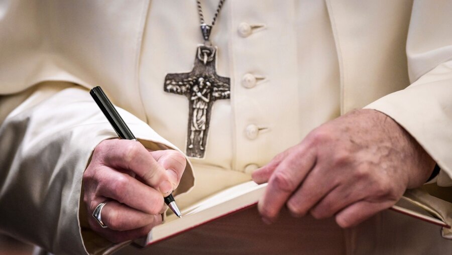 Papst Franziskus schreibt mit einem Kugelschreiber in ein Heft mit weißen Seiten  / © Cristian Gennari/Romano Siciliani (KNA)