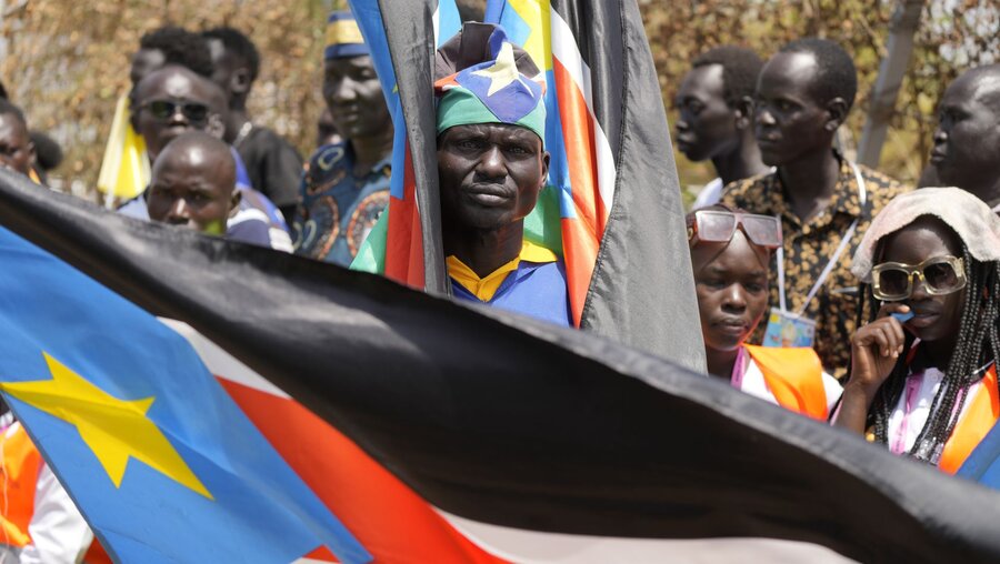 Papst-Reise in den Südsudan: Menschen tragen Nationalfahnen während sie vor dem Tor des Flughafens auf die Ankunft des Papstes warten / © Ben Curtis/AP (dpa)