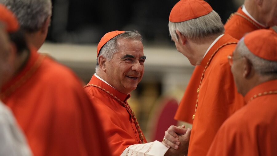 Kardinal Angelo Becciu (M) gibt einem anderen Kardinal die Hand, während er am Konsistorium im Petersdom teilnimmt / © Andrew Medichini (dpa)