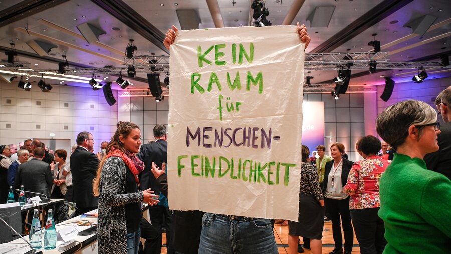 Eine Teilnehmerin hält ein Transparent hoch mit der Aufschrift: Kein Raum für Menschenfeindlichkeit, als Protest nach einer Abstimmung der Bischöfe während der vierten Synodalversammlung am 8. September 2022 in Frankfurt. / © Julia Steinbrecht (KNA)