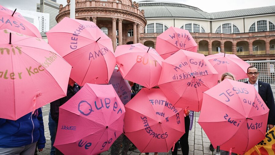 Menschen halten offene Regenschirme in der Farbe pink, die handschriftlich mit Protestparolen beschriftet sind, während der vierten Synodalversammlung / © Julia Steinbrecht (KNA)