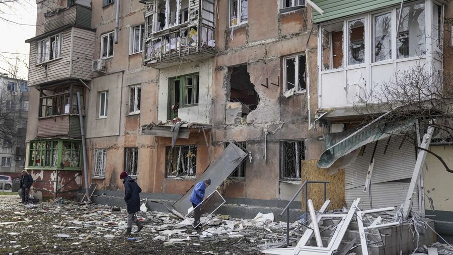 Ukraine: Menschen gehen an einem von Granaten getroffenen Wohnhaus vorüber / © Evgeniy Maloletka (dpa)