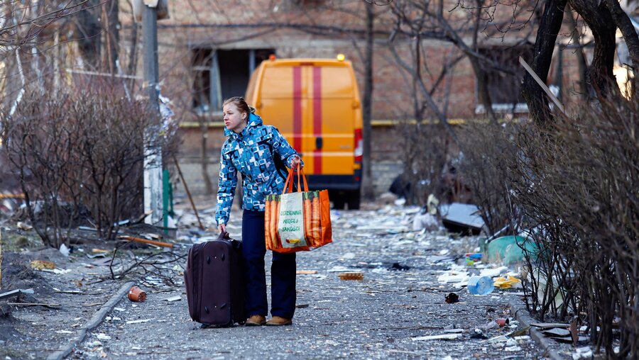 Eine Frau verlässt am 18.03.2022 mit ihren wenigen Habseligkeiten ein Wohnhaus, das durch einen russischen Angriff zerstört wurde. / © Mohammad Javad Abjoushak/SOPA Images via ZUMA Press Wire (dpa)