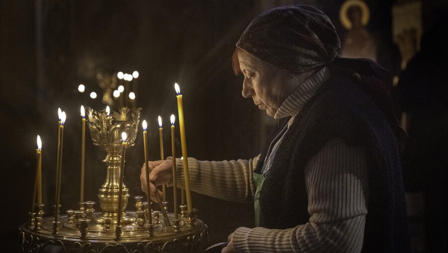Eine Frau zündet Kerzen in der St.-Andreas-Kirche in Kiew an. / © Mark Edward Harris (dpa)