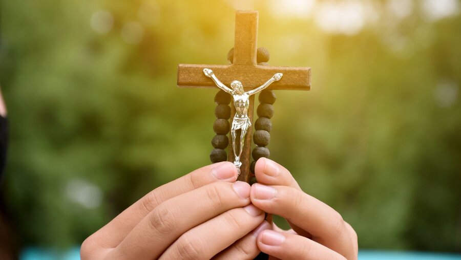 Zwei Hände halten ein hölzernes Kreuz mit Rosenkranz / © Sophon Nawit (shutterstock)