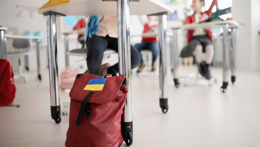 Ein Rucksack mit einem Aufkleber in den Farben der ukrainischen Flagge in einem Klassenraum / © Halfpoint (shutterstock)
