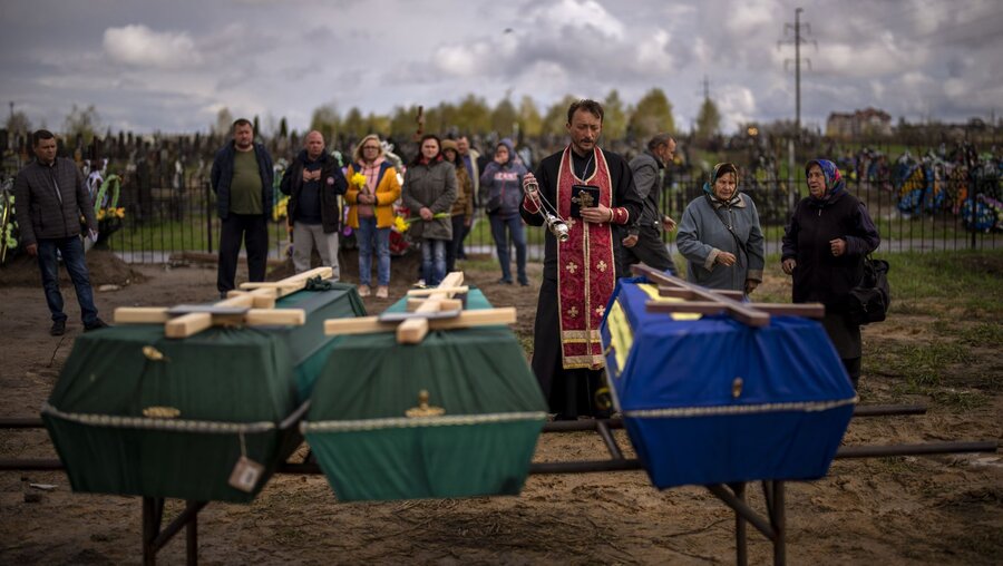 Ukraine, Butscha: Ein Priester segnet drei Verstorbene, die während der russischen Besatzung starben und aus provisorischen Gräbern in Butscha exhumiert wurden / © Emilio Morenatti (dpa)