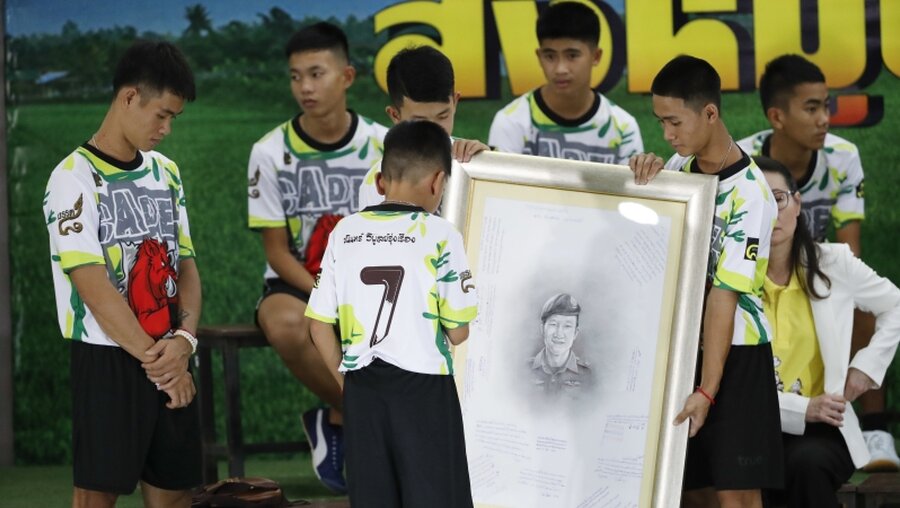 Jungen der geretteten Fußballmannschaft mit einem Bild des Tauchers, der bei der Rettung ums Leben kam / © Vincent Thian (dpa)