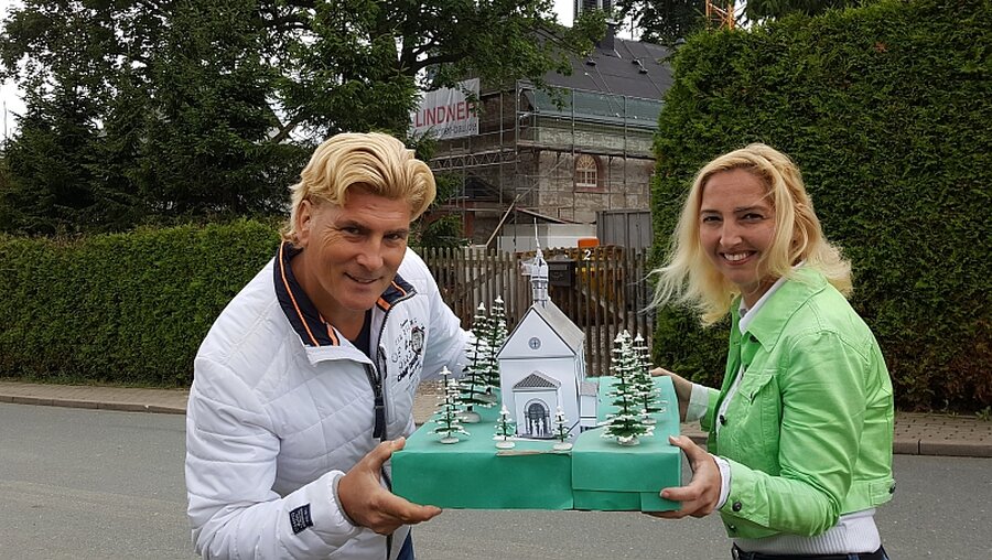 Vivienne und Tino Taubert mit dem Modell ihrer Kirche, das fast fertige Original im Hintergrund / © Doreen Reinhard (privat)