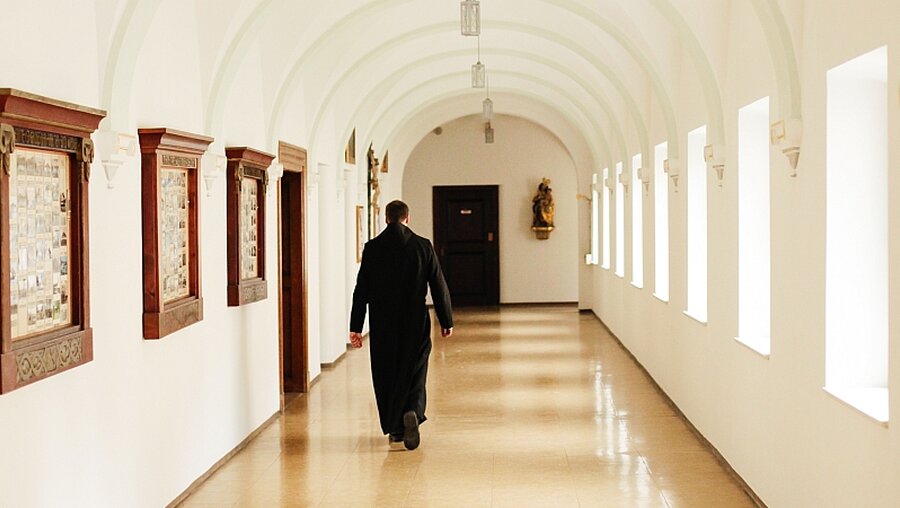 Ein Benediktiner geht durch einen Klosterflur / © Simon Koy (KNA)