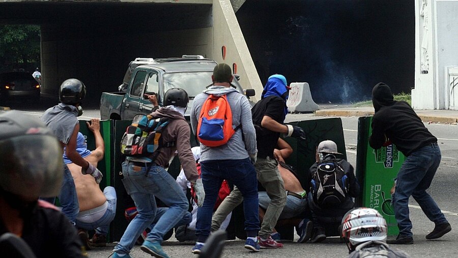 Demonstranten versuchen sich während eines Protests am 26.04.2017 in Caracas (Venezuela) vor Tränengas zu schützen / © José Cohen (dpa)