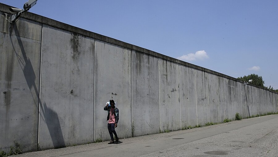 Mailand: Ein Mann geht an der Mauer eines Flüchtlingslagers außerhalb von Mailand entlang. / ©  Luca Bruno (dpa)