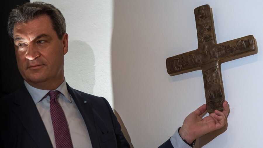 Markus Söder, Bayerischer Ministerpräsident (CSU), hängt ein Kreuz im Eingangsbereich der bayerischen Staatskanzlei auf. / © Peter Kneffel (dpa)