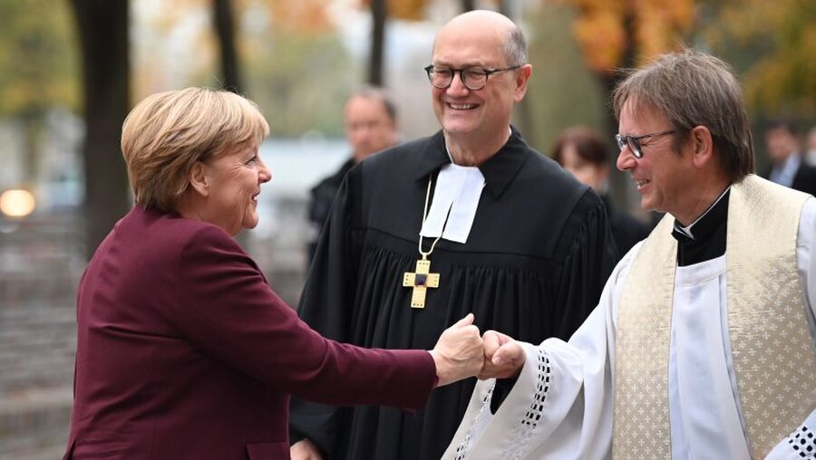 Martin Dutzmann (M) und Prälat Karl Jüsten (r) empfangen Angela Merkel zum ökumenischen Gottesdienst / © Britta Pedersen (dpa)