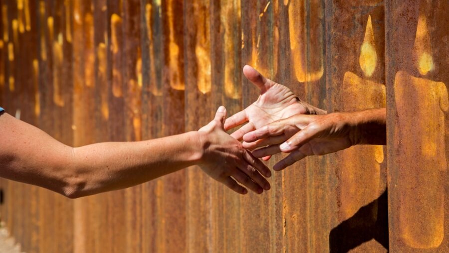 Menschen reichen sich durch einen Zaun die Hände / © Jim West (KNA)