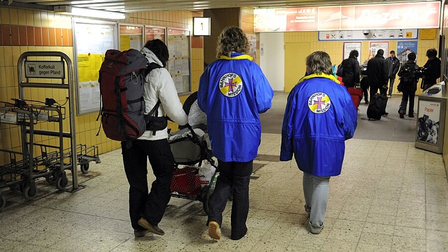 Mitarbeiterinnen der Bahnhofsmission helfen einer Frau mit Kinderwagen beim Umsteigen (KNA)