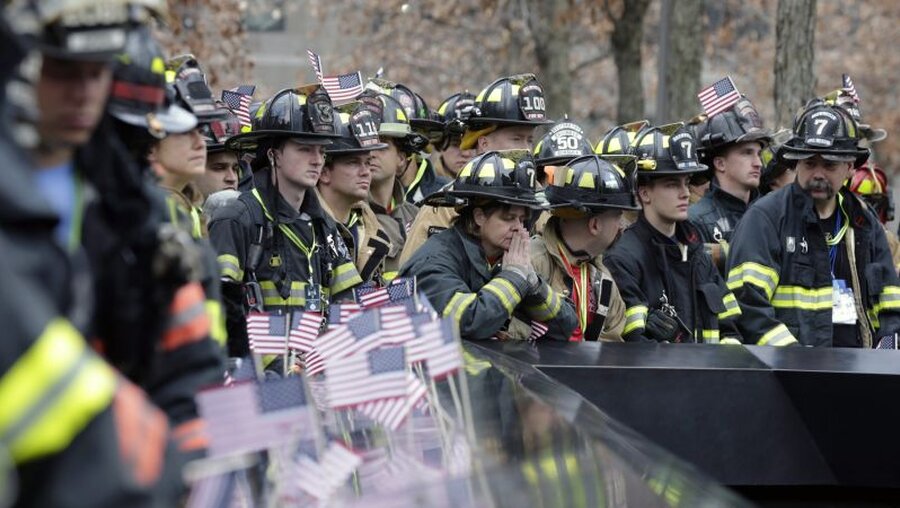 New York: Eine Feuerwehrfrau (M) spricht ein Gebet neben anderen Feuerwehrleuten / © Jason Szenes (dpa)